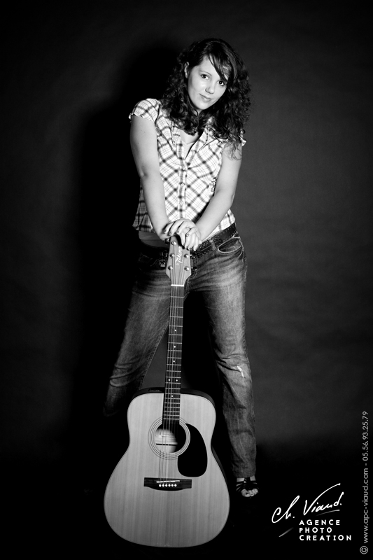 Photo en noir et blanc d'une femme tenant sa guitare dans un studio photos